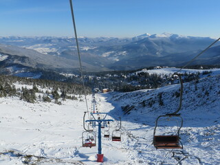 Fototapeta premium mountains in winter, ski slope and chairlift, view of the village among the winter forest in the mountains