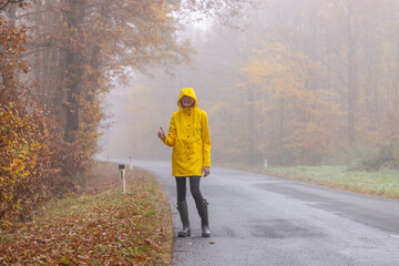 Young woman with yellow raincoat and rubber boots in autumn landscape
