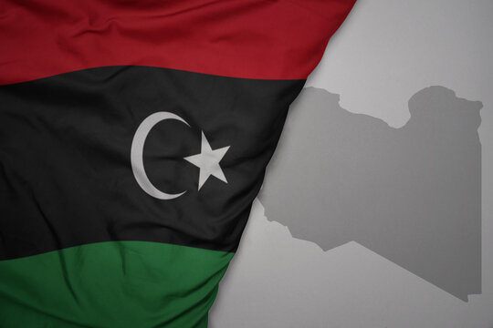 big waving national colorful flag and map of libya on the gray background.