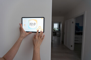 Woman controlling home with a digital touch screen panel installed on the wall in the living room