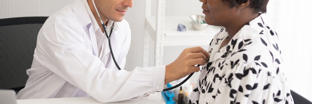 Hispanic physician check-up African American patient with stethoscope at the hospital. Healthcare medical diagnosis and examining on the laptop. Copy space background.