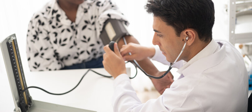Hispanic doctor measuring African American patient's blood pressure. Person medical healthcare and wellbeing, the physician meet with patient at clinic concept. - Powered by Adobe