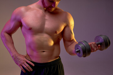 Fototapeta na wymiar sporty well-built man with dumbbell in hand, guy takes part in challenge, changing body process, isolated brown background, cropped shot, focus on strong perfect body