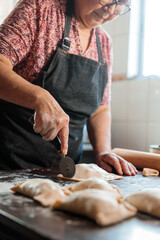 Latin mature Woman using dough cutter knife for Preparing Chilean Beef Empanadas in Her Home Kitchen