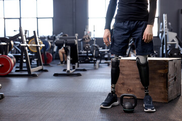 cropped shot of body of disabled man with prosthetic leg standing in modern gym preparing for weight training. copy space, blurred background. strength health care - obrazy, fototapety, plakaty