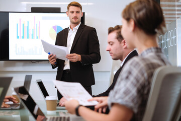 Handsome young caucasian businessman presents graph and data of new business performance in meeting room.