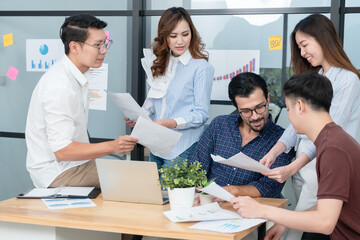 Diverse employees in office brainstorming while discussing ideas for new project, using laptop. Multiracial coworkers gather in meeting room discuss ideas in group of business people