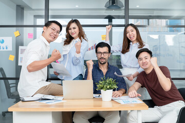 Young business men and women in casual wear celebrate success with laptop in office. Diversity successful business people raising fists with happy face, looking at camera. Coworker teamwork
