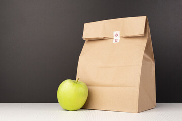 Traditional paper lunch bag for students with an apple on the background of the blackboard