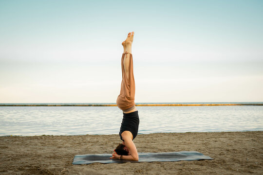 "Woman Attempting a Headstand on a Black Mat in the Park, Practicing Yoga After Work