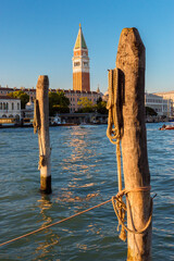 Piazza San Marco, Venice, Italy, Romantic walk in Venice at sunshine. Wooden stakes on the canal grande in venice. St Mark’s Square Campanile in the background. - obrazy, fototapety, plakaty