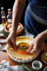 Preparing a spiral tart, rolling thin slices of vegetables into a tight spiral in the center of the tart, focus on  inside, close-up view