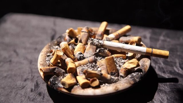 Cigarettes burning in ashtray full of cigarette butts