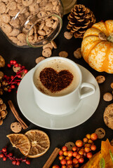 Autumn-themed composition with cup of coffee in the middle, decorated with coco heart. Autumn leaves, pumpkin, jar of cookies. 