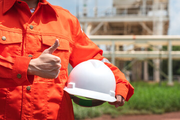 Action of the engineer in orange coverall uniform is holding a white safety helmet with background...