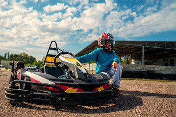 girl racer posing near a racing kart on the track in a helmet