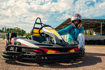 girl racer posing near a racing kart on the track in a helmet