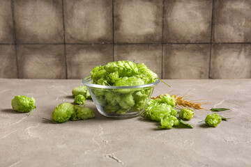 Glass bowl with fresh green hops and wheat on grey table