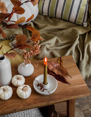 A lit candle on a wooden bench with autumn decor near the sofa - obrazy, fototapety, plakaty