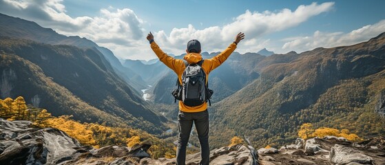 Back view of a young Asian hiker standing and raising his hands in happiness on the summit of a rough mountain, copy space. - obrazy, fototapety, plakaty