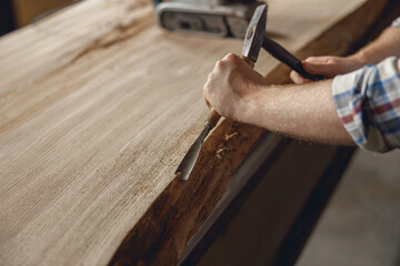 Close up of craftsman working with chisel while cutting wooden plank in carpentry workshop