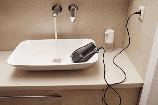 Electrical shock can occur in the bathroom. An electrical appliance lies dangerously in a sink with running water