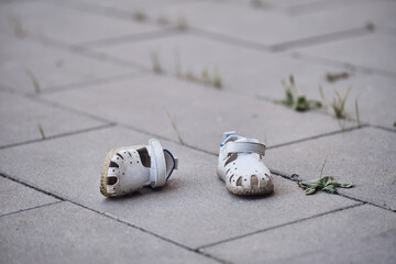 Pair of white baby shoes on the pavement, lost children boots