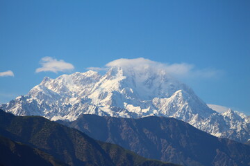 Under the blue sky, the mountains are covered with snow and clouds are circling the mountain