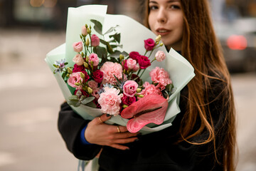 Woman holding flower bouquet of eustoma, carnations, anthurium and eucalyptus wrapped in mint color...