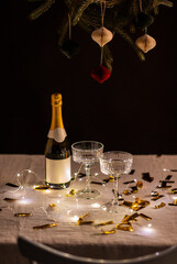 christmas, celebration and winter holidays concept - champagne in glasses, electric garland lights and golden confetti on table over black background