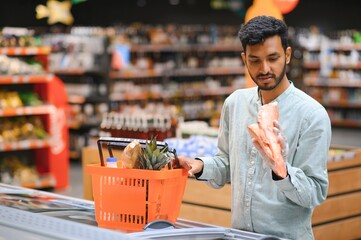 Portrait of happy handsome young Indian at grocery shop or supermarket. - obrazy, fototapety, plakaty