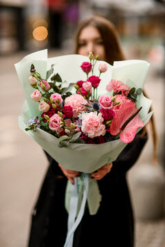 Selective focus of delicate flower bouquet of eustoma, carnations, anthurium and eucalyptus in red and pink colors in woman's hands