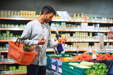 Closeup portrait, handsome young man picking up bell peppers, choosing yellow and orange vegetables in grocery store