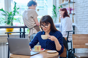 Middle aged woman in bakery with cup of coffee and dessert cake