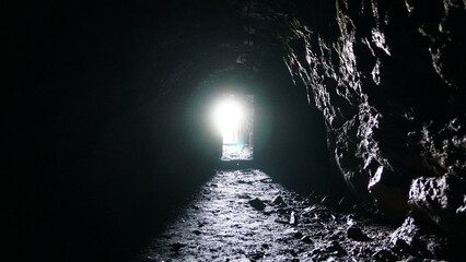 Light and exit at the end of the wet cave. The rays of the sun fall on the stone damp walls. An...