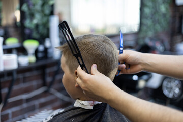 In a hairdressing salon, a child sits in a chair and carefully observes the work of a hairdresser. The child loves to get a haircut and is not afraid of the hairdresser. Haircut concept.
