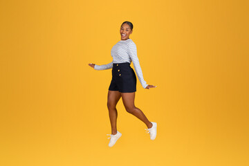 Fototapeta na wymiar Excited young black woman jumping in the air on yellow