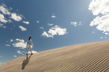 woman in the desert walking among dunes at sunset with the sun against the sky, copy space in the sky