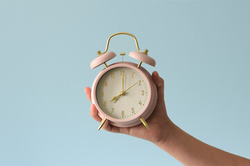 An alarm clock in the hand of a child. The girl holds a pink mechanical alarm clock from...