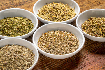 herb spices - dried leaves of parsley, rosemary, thyme, oregano and basil, collection of small ceramic bowls on a rustic wood