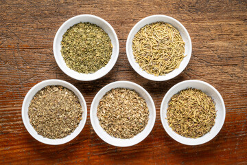 Obraz na płótnie Canvas herb spices - dried leaves of parsley, rosemary, thyme, oregano and basil, collection of small ceramic bowls on a rustic wood, top view
