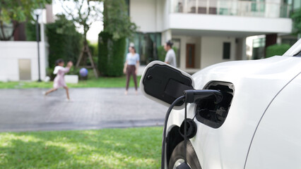 Progressive parent have returned from picking up daughter at school with concept of electric vehicle and renewable energy, charging station for EV car at home. Alternative eco transportation.