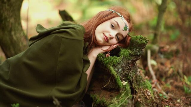 Beautiful red haired girl with tiara in medieval dress. Fairy tale story about princess.Amazing model in forest laying on tree with moss.Warm art work