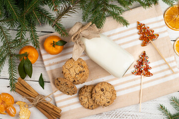 milk and cookies on the table with spruce branches, christmas treats for Santa Claus, tangerines, cinnamon, christmas traditions, flat lay