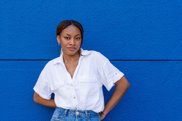 Young pretty black ethnic woman wearing white shirt looking at the camera on a blue color background.