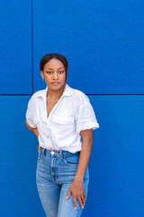 Pretty young woman of black ethnicity in white shirt looking at the camera defiantly, with a blue color background.