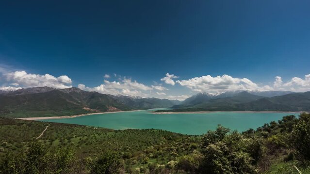 Mountains and lake video timelapse for background. View of lake or reservoir Charvak in mountains. Cumulus clouds swirl over mountains. Blue sky over turquoise water surface. Joyful peaceful cinematic