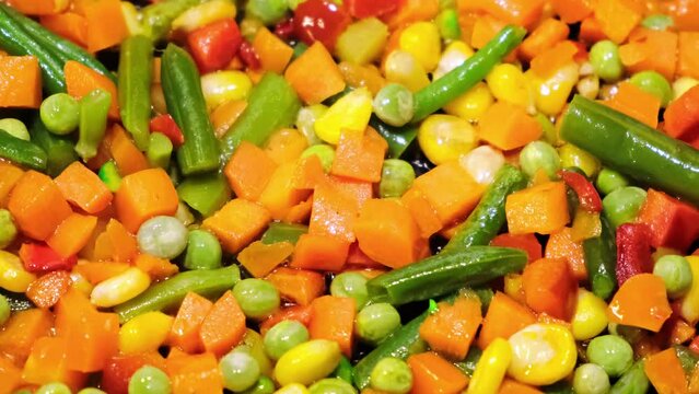 Cooking of frozen traditional mexican vegetable mix. Mixing with a spatula. Frying of carrots, green beans, corns. Melting ice on hot pan. Fast healthy food. Vegan dish. Bright colorful ingredients.