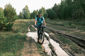 Fototapeta na wymiar man wearing sports gloves and carrying a backpack rides a mountain bike through a puddle in a forest area.Active lifestyle