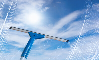 Rubber squeegee cleans a soaped window and clears a stripe of bright blue sky, spring cleaning...